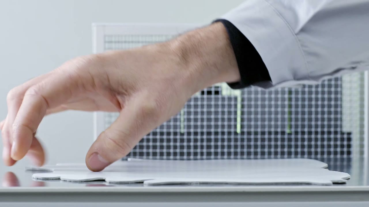 Still from Adidas x Prada: a pale hand reaching across a white desk in a sterile white room